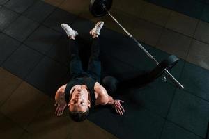 Top view of strong man in sportive clothes that sitting on the floor and takes a break in the gym photo