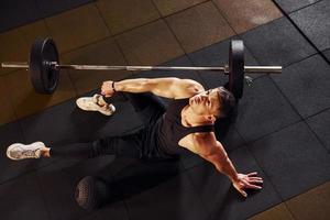 Top view of strong man in sportive clothes that sitting on the floor and takes a break in the gym photo