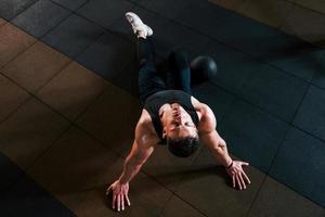 vista superior de un hombre fuerte con ropa deportiva que se sienta en el suelo y toma un descanso en el gimnasio foto