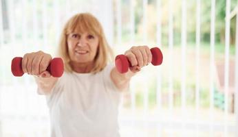 anciana positiva con ropa deportiva en el interior durante el día haciendo ejercicios con pesas foto