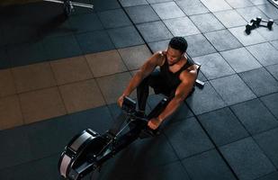 un hombre afroamericano fuerte con ropa deportiva tiene un día de entrenamiento en el gimnasio y usa equipo. concepto de poder y fuerza foto