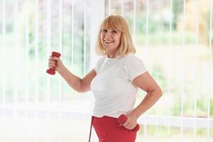 anciana positiva con ropa deportiva en el interior durante el día haciendo ejercicios con pesas foto