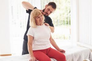 Older woman have a visit in clinic and having rehabilitation. Male instructor helping her photo