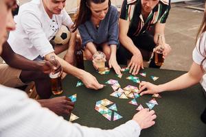 Playing card game. Group of young people in casual clothes have a party at rooftop together at daytime photo