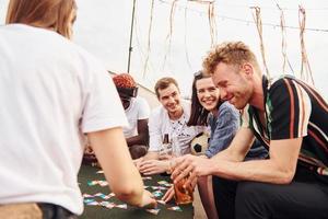 Playing card game. Group of young people in casual clothes have a party at rooftop together at daytime photo