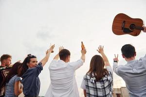 de pie alto y mirando el cielo nublado. un grupo de jóvenes con ropa informal tienen una fiesta en la azotea juntos durante el día foto