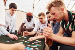 Playing card game. Group of young people in casual clothes have a party at rooftop together at daytime photo