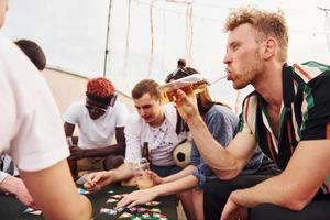 Playing card game. Group of young people in casual clothes have a party at rooftop together at daytime photo