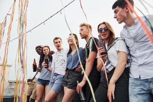 apoyándose en el borde de la azotea con decoraciones. grupo de jóvenes con ropa informal tienen una fiesta juntos durante el día foto