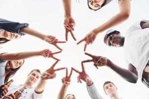 Making beautiful gesture by fingers. View from below. Group of young people in casual clothes have a party at rooftop together at daytime photo