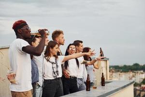 de pie alto con el alcohol. cielo nublado. un grupo de jóvenes con ropa informal tienen una fiesta en la azotea juntos durante el día foto