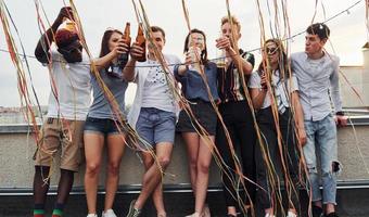 apoyándose en el borde de la azotea con decoraciones. grupo de jóvenes con ropa informal tienen una fiesta juntos durante el día foto