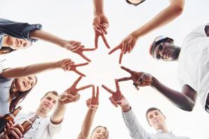 Making beautiful gesture by fingers. View from below. Group of young people in casual clothes have a party at rooftop together at daytime photo