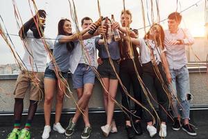 Leaning on the edge of the rooftop with decorates. Group of young people in casual clothes have a party together at daytime photo