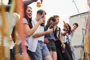 Leaning on the edge of the rooftop with decorates. Group of young people in casual clothes have a party together at daytime photo