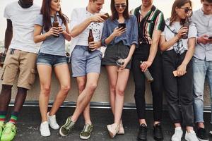 Standing with alcohol at the edge of rooftop. Group of young people in casual clothes have a party together at daytime photo