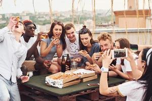Making photo. Delicious pizza. Group of young people in casual clothes have a party at rooftop together at daytime photo