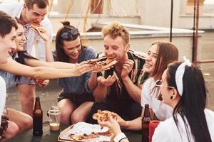 Delicious pizza. Group of young people in casual clothes have a party at rooftop together at daytime photo