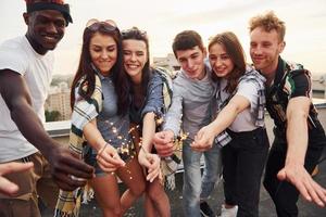 With sparklers in hands. Group of young people in casual clothes have a party at rooftop together at daytime photo