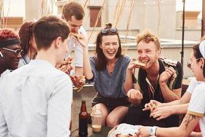 Delicious pizza. Group of young people in casual clothes have a party at rooftop together at daytime photo