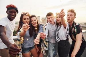 With sparklers in hands. Group of young people in casual clothes have a party at rooftop together at daytime photo