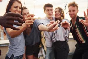 With sparklers in hands. Group of young people in casual clothes have a party at rooftop together at daytime photo