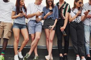 Standing with alcohol at the edge of rooftop. Group of young people in casual clothes have a party together at daytime photo