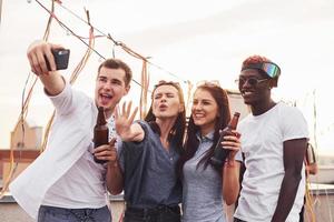 Standing together and taking selfie. Group of young people in casual clothes have a party at rooftop together at daytime photo