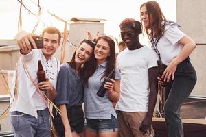 Standing together and taking selfie. Group of young people in casual clothes have a party at rooftop together at daytime photo