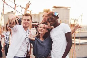 Standing together and taking selfie. Group of young people in casual clothes have a party at rooftop together at daytime photo