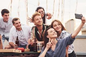 Making photo. Delicious pizza. Group of young people in casual clothes have a party at rooftop together at daytime photo