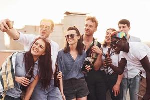 haciendo selfie por teléfono. un grupo de jóvenes con ropa informal tienen una fiesta en la azotea juntos durante el día foto