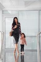 joven madre con su hija caminando juntos en el interior de la oficina o el aeropuerto. teniendo vacaciones foto
