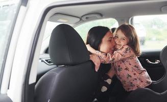 abrazándose unos a otros. madre con su hija dentro de un automóvil moderno juntos foto