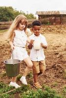 Holding milk. Cute little african american boy with european girl is on the farm photo