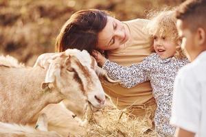 Young mother with her daughter is on the farm at summertime with goats photo