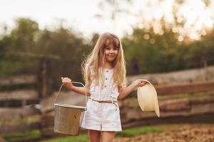 niñita vestida de blanco está en la granja en verano al aire libre con leche foto