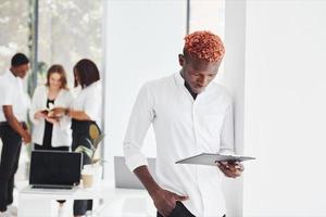 Man with notepad standing in front of colleagues. Group of african american business people working in office together photo