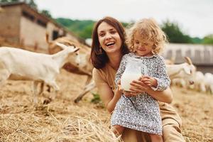 Fresh natural milk. Young mother with her daughter is on the farm at summertime with goats photo