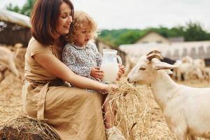 Fresh natural milk. Young mother with her daughter is on the farm at summertime with goats photo