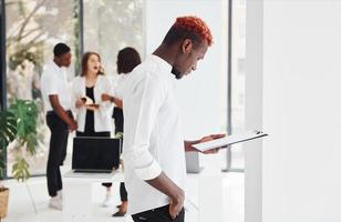 Man with notepad standing in front of colleagues. Group of african american business people working in office together photo