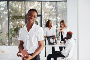 Positive guy standing in front of his colleagues. Group of african american business people working in office together photo