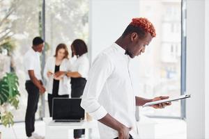 Man with notepad standing in front of colleagues. Group of african american business people working in office together photo