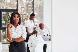 Beautiful woman in glasses in front of her colleagues. Group of african american business people working in office together photo