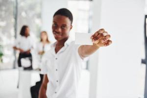 Positive guy standing in front of his colleagues. Group of african american business people working in office together photo