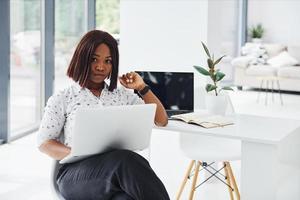 Young african american woman in formal clothes is in the office with laptop photo