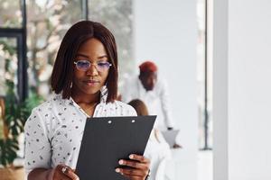 Beautiful woman in glasses in front of her colleagues. Group of african american business people working in office together photo