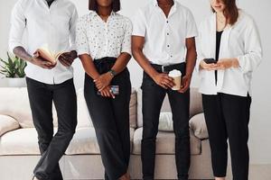 Group of african american people in formal clothes standing near sofa indoors in office together photo