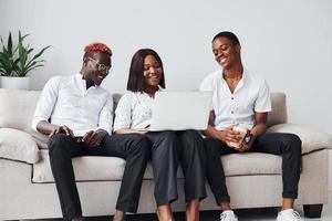cómodo sofá. usando una computadora portátil grupo de empresarios afroamericanos que trabajan sentados juntos foto