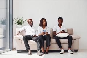 Group of african american people in formal clothes sitting on sofa indoors in office together photo